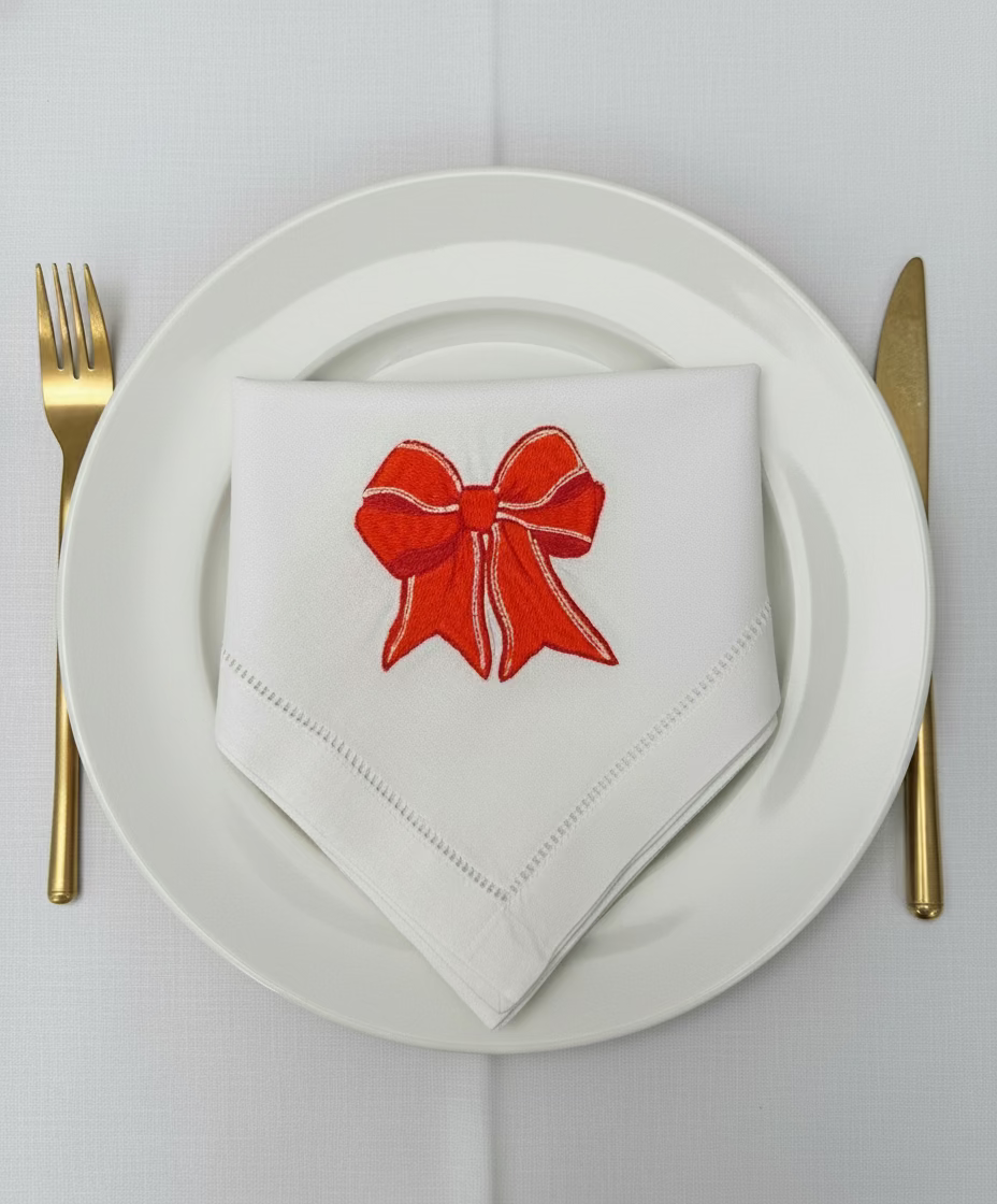 Napkin with red bow design on a white plate with gold fork and knife on wooden table